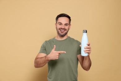 Happy man pointing on thermo bottle against beige background
