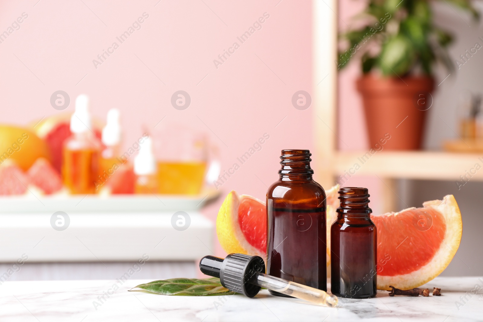 Photo of Bottles of essential oil and grapefruit slices on table against blurred background. Space for text
