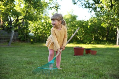 Cute little girl with rake in garden on spring day