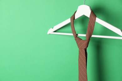 Photo of Hanger with brown striped tie on green background. Space for text