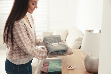 Photo of Woman with scented sachet and clothes near chest of drawers in room