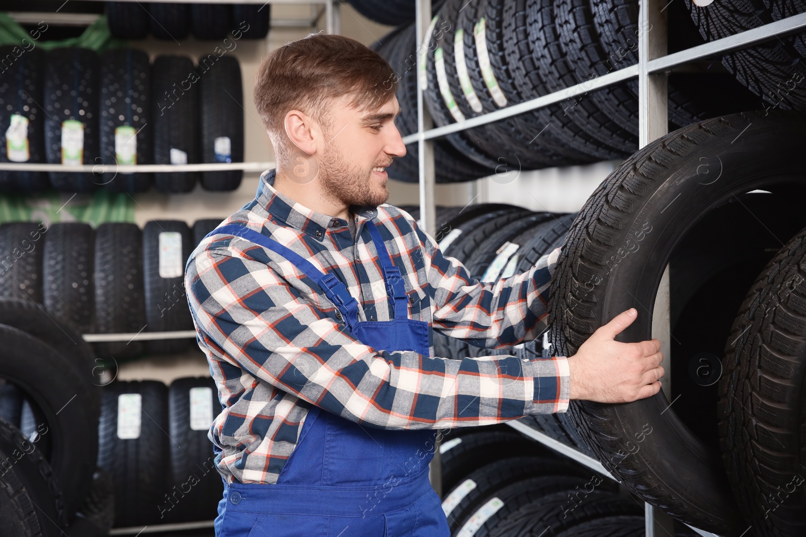 Photo of Young male mechanic with car tires in automobile service center