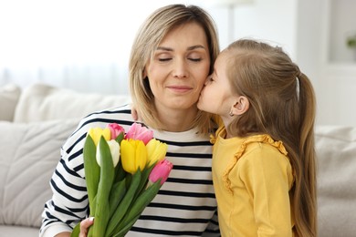 Little daughter kissing and congratulating her mom with Mother`s Day at home. Woman holding bouquet of beautiful tulips