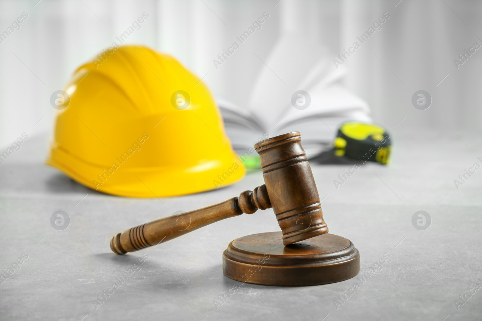 Photo of Construction and land law concepts. Judge gavel, protective helmet, tape measure with open book on light grey table