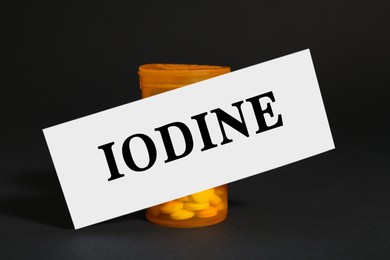 Photo of Paper note with word Iodine and bottle of pills on black background