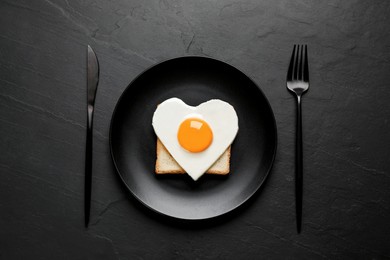Photo of Tasty fried egg in shape of heart with toast served on black table, flat lay