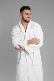 Happy young man in bathrobe on grey background