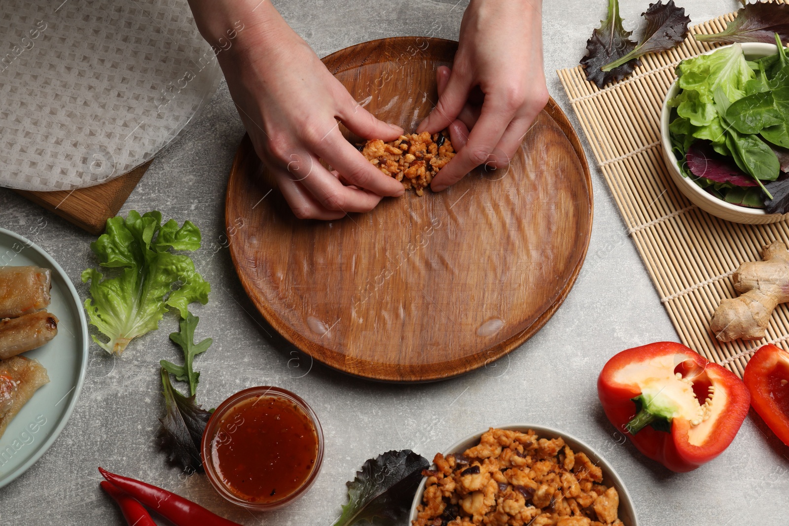 Photo of Woman making tasty spring roll at grey table, top view