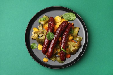 Photo of Delicious smoked sausage and baked vegetables on green background, top view