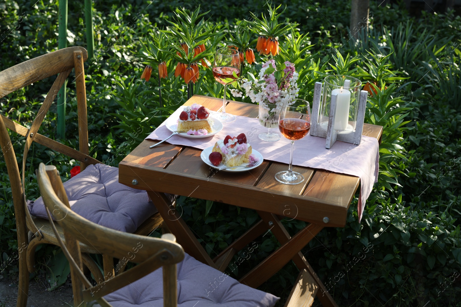 Photo of Vase with spring flowers, wine and cake on table served for romantic date in garden