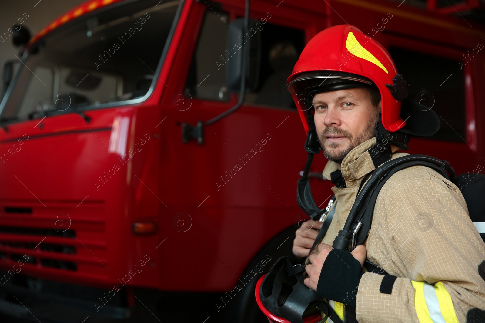 Photo of Portrait of firefighter in uniform near red fire truck at station, space for text