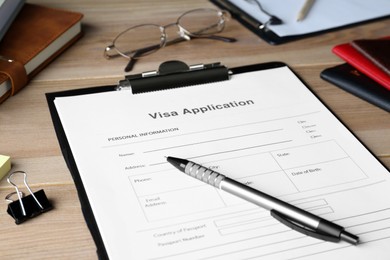 Photo of Visa application form for immigration and stationery on wooden table, closeup