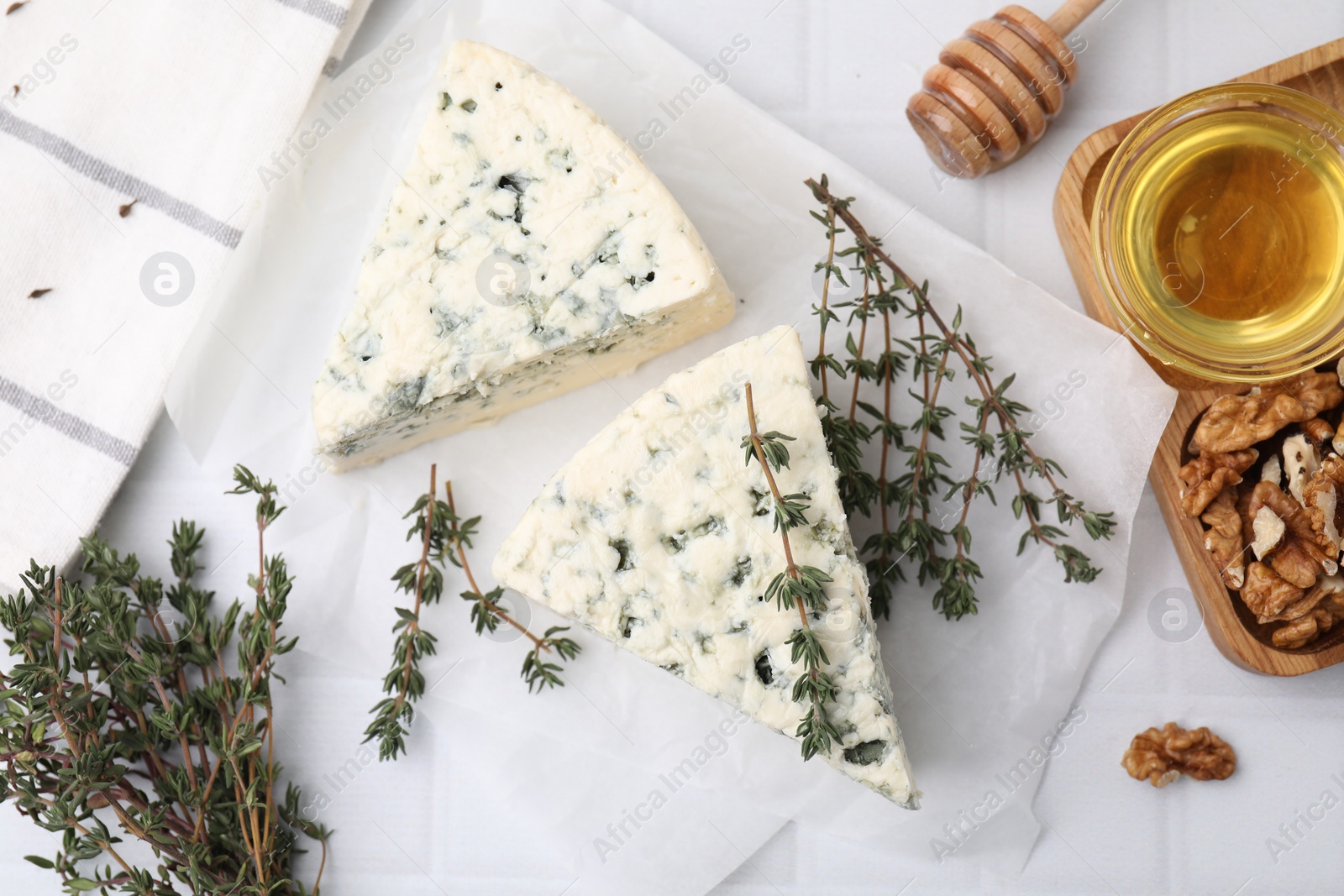 Photo of Tasty blue cheese with thyme, walnuts and honey on white tiled table, flat lay