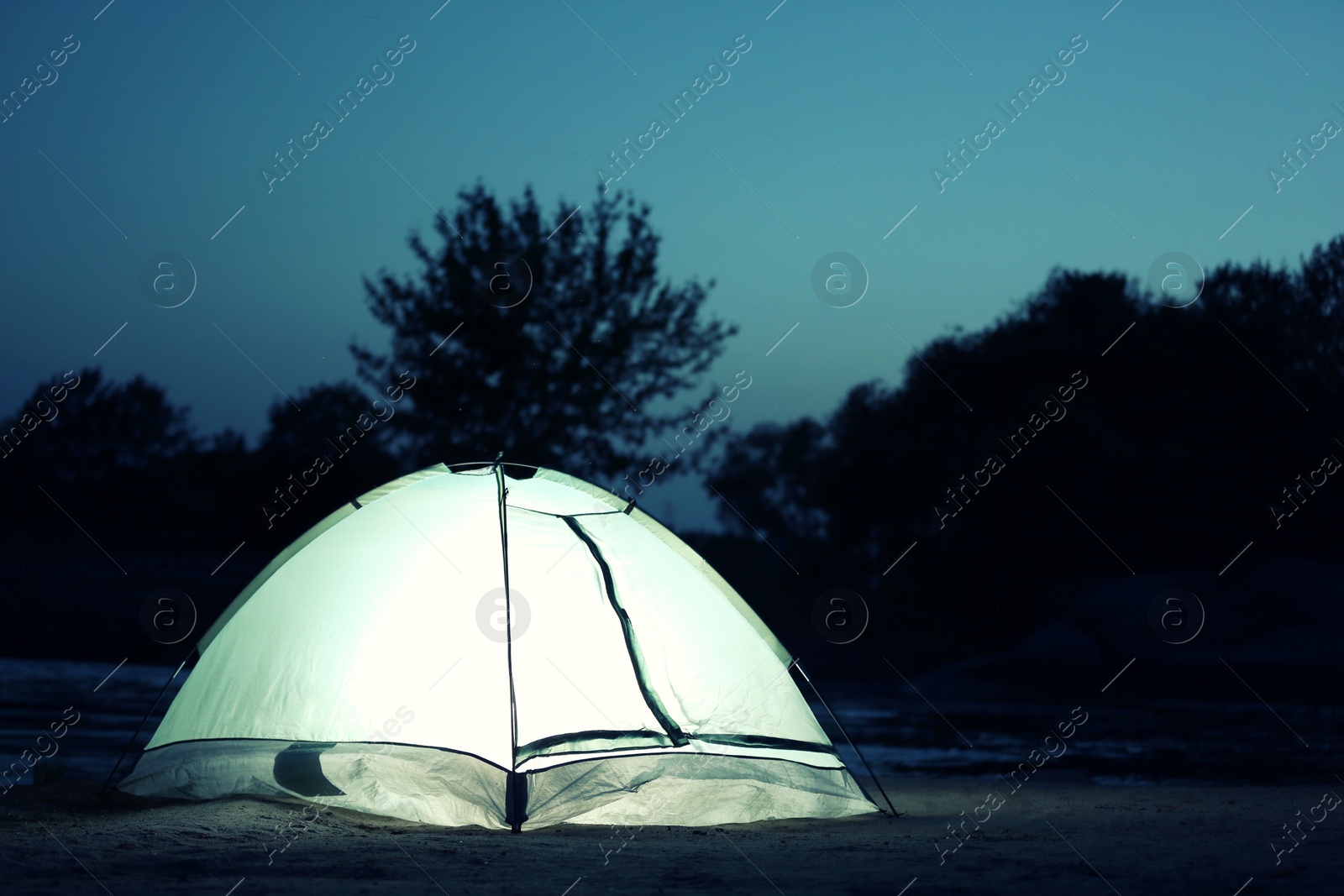 Photo of Small camping tent glowing in twilight outdoors. Space for text