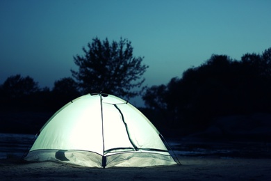 Photo of Small camping tent glowing in twilight outdoors. Space for text