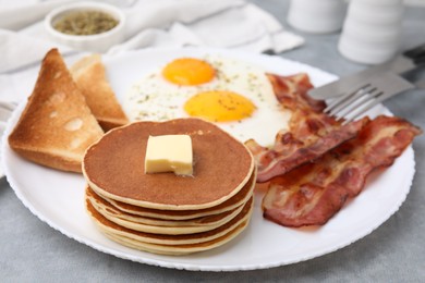Photo of Tasty pancakes served with fried eggs and bacon on grey table, closeup
