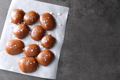 Photo of Tasty caramel candies and salt on grey table, top view. Space for text