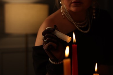 Woman with elegant jewelry lightning up candle indoors, closeup