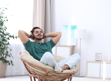 Photo of Handsome young man listening music in armchair at home. Space for text