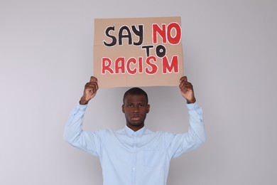 Photo of African American man holding sign with phrase Say No To Racism on light background