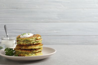 Delicious zucchini fritters with sour cream on grey table. Space for text