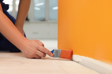 Photo of Worker using brush to paint wall with orange dye indoors, closeup