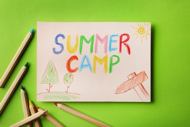 Paper with written text SUMMER CAMP, drawings and different pencils on color background, flat lay