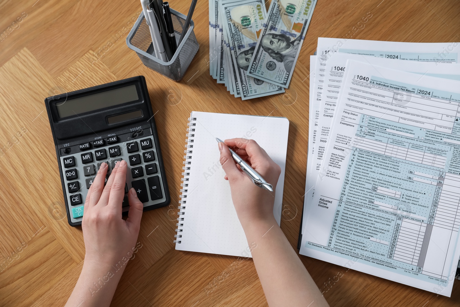 Photo of Payroll. Woman using calculator while taking notes in notebook at wooden table, top view