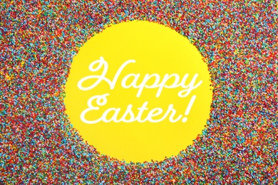 Image of Text Happy Easter and frame of colorful sprinkles on yellow background, top view. Confectionery decor