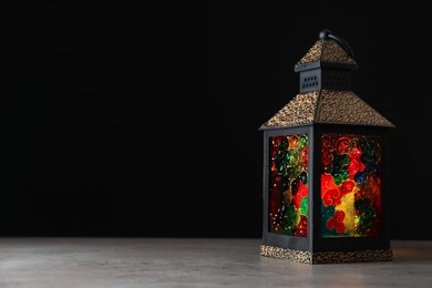Photo of Decorative Arabic lantern on grey table against black background, space for text