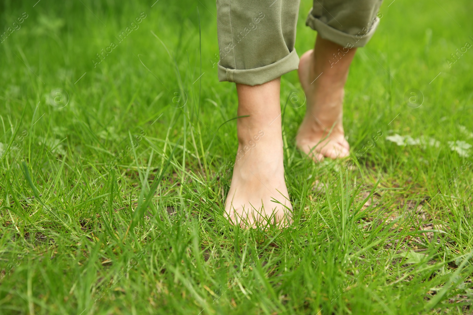 Photo of Woman walking barefoot on green grass outdoors, closeup