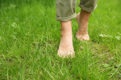 Photo of Woman walking barefoot on green grass outdoors, closeup