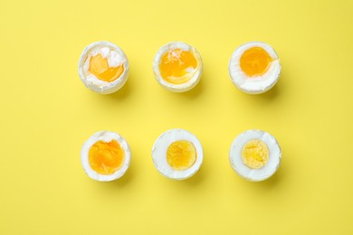 Photo of Different readiness stages of boiled chicken eggs on yellow background, flat lay
