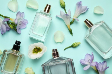 Photo of Flat lay composition of different perfume bottles and flowers on cyan background