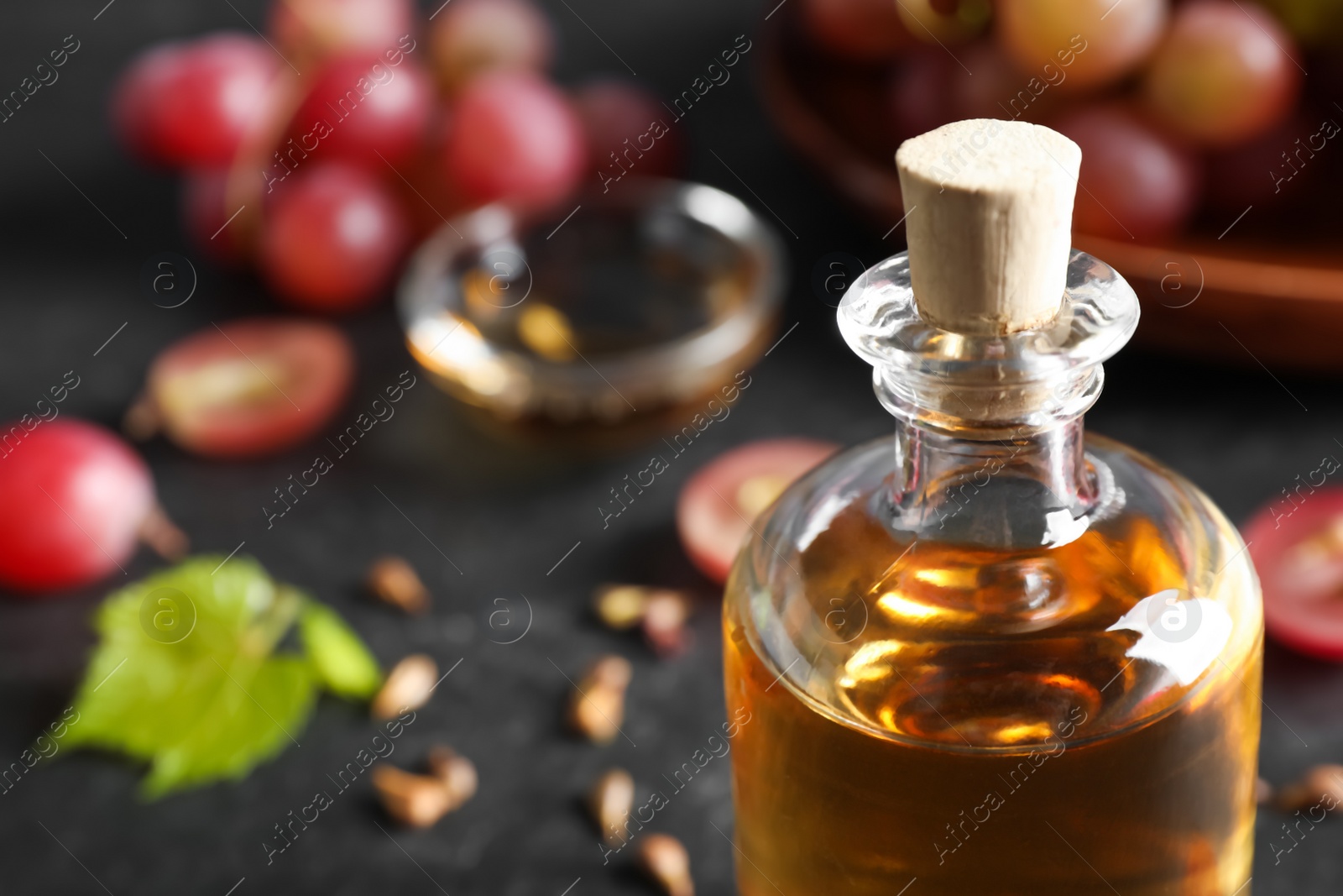 Photo of Bottle of natural grape seed oil on black table, closeup with space for text. Organic cosmetic