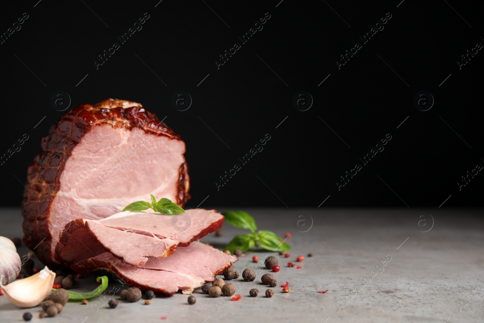 Photo of Delicious ham with spices, garlic and basil on grey table against black background, space for text