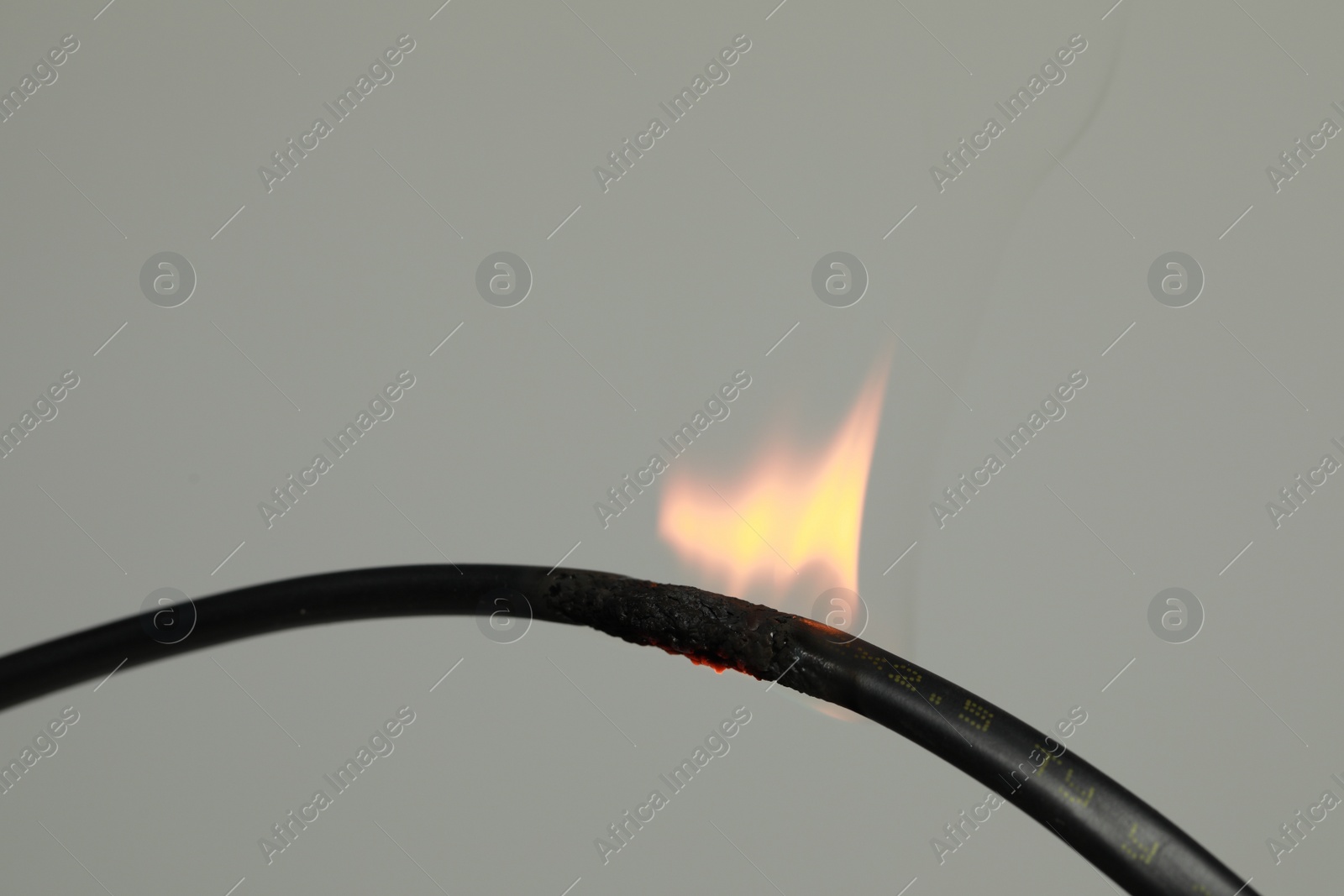 Photo of Inflamed black wire on grey background, closeup. Electrical short circuit