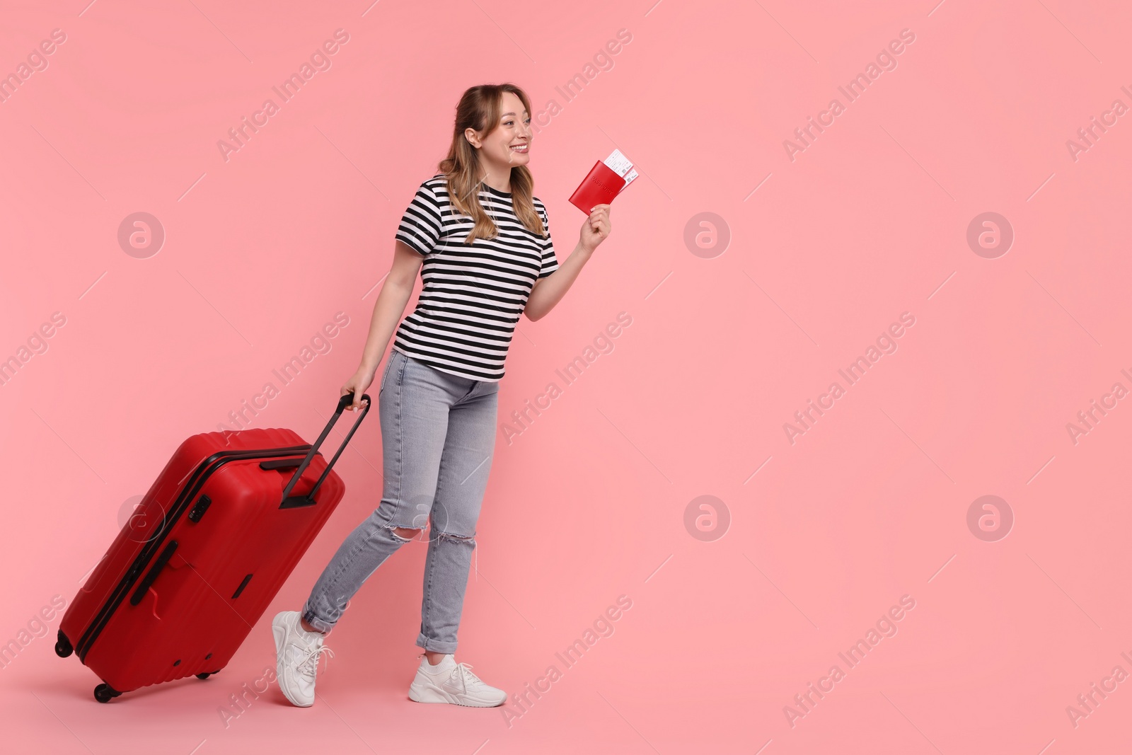 Photo of Happy young woman with passport, ticket and suitcase on pink background, space for text