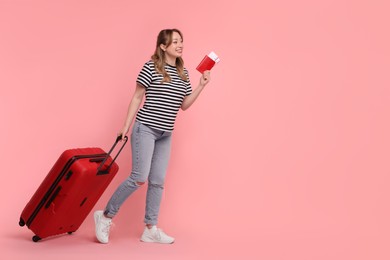 Happy young woman with passport, ticket and suitcase on pink background, space for text