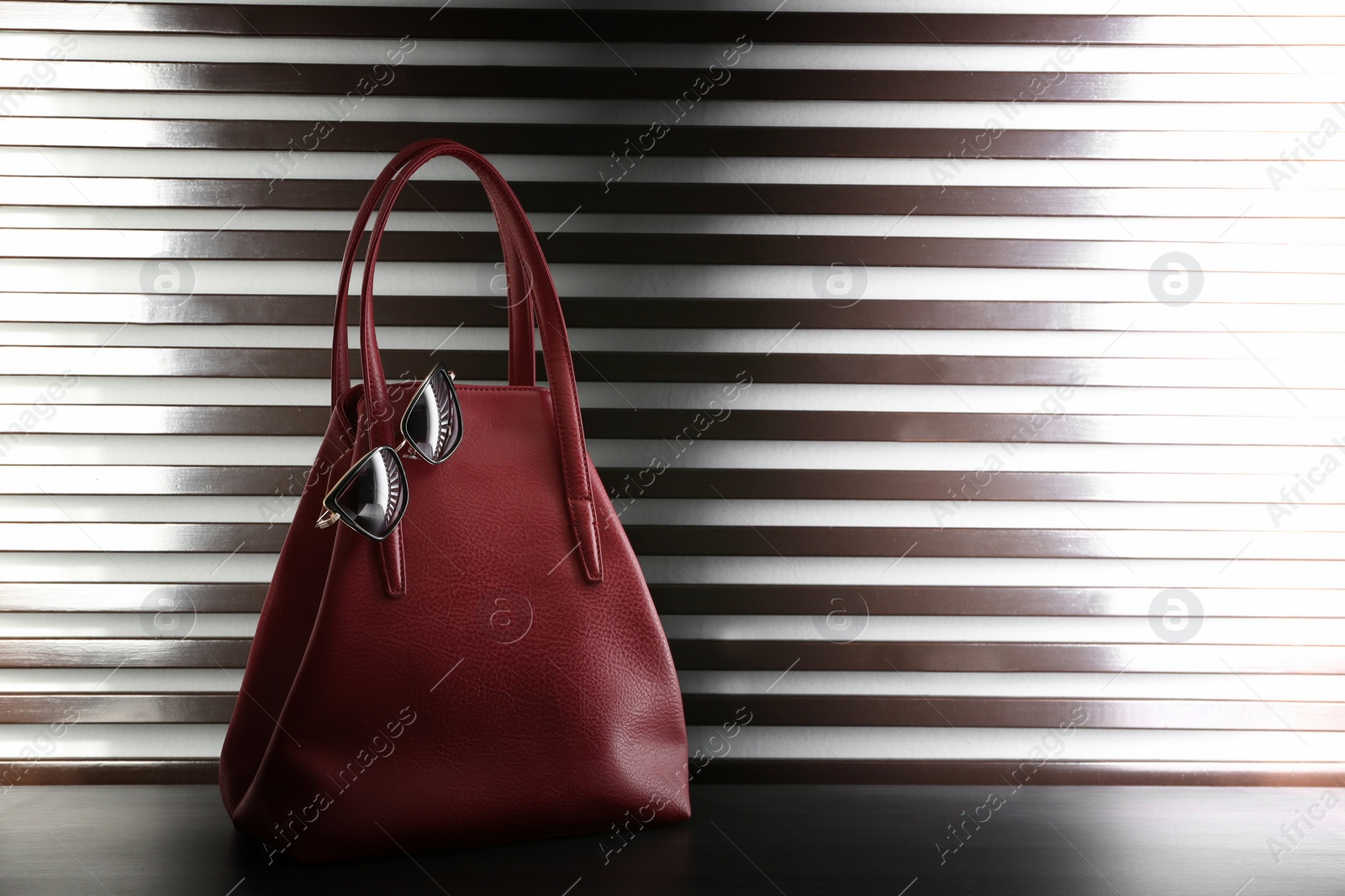 Photo of Stylish woman's bag and sunglasses on dark grey table. Space for text