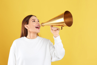 Young woman with vintage megaphone on yellow background