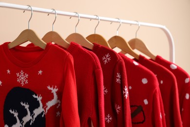 Rack with different Christmas sweaters on beige background, closeup