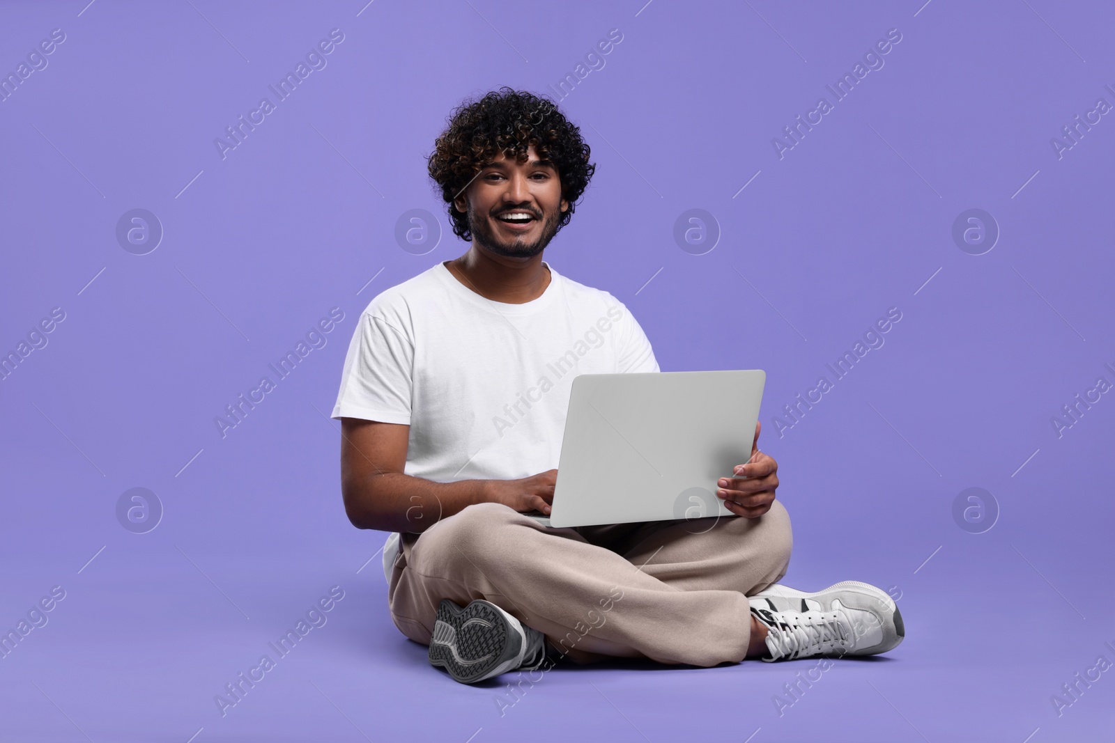 Photo of Happy man with laptop on purple background, space for text