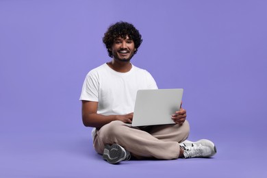 Happy man with laptop on purple background, space for text