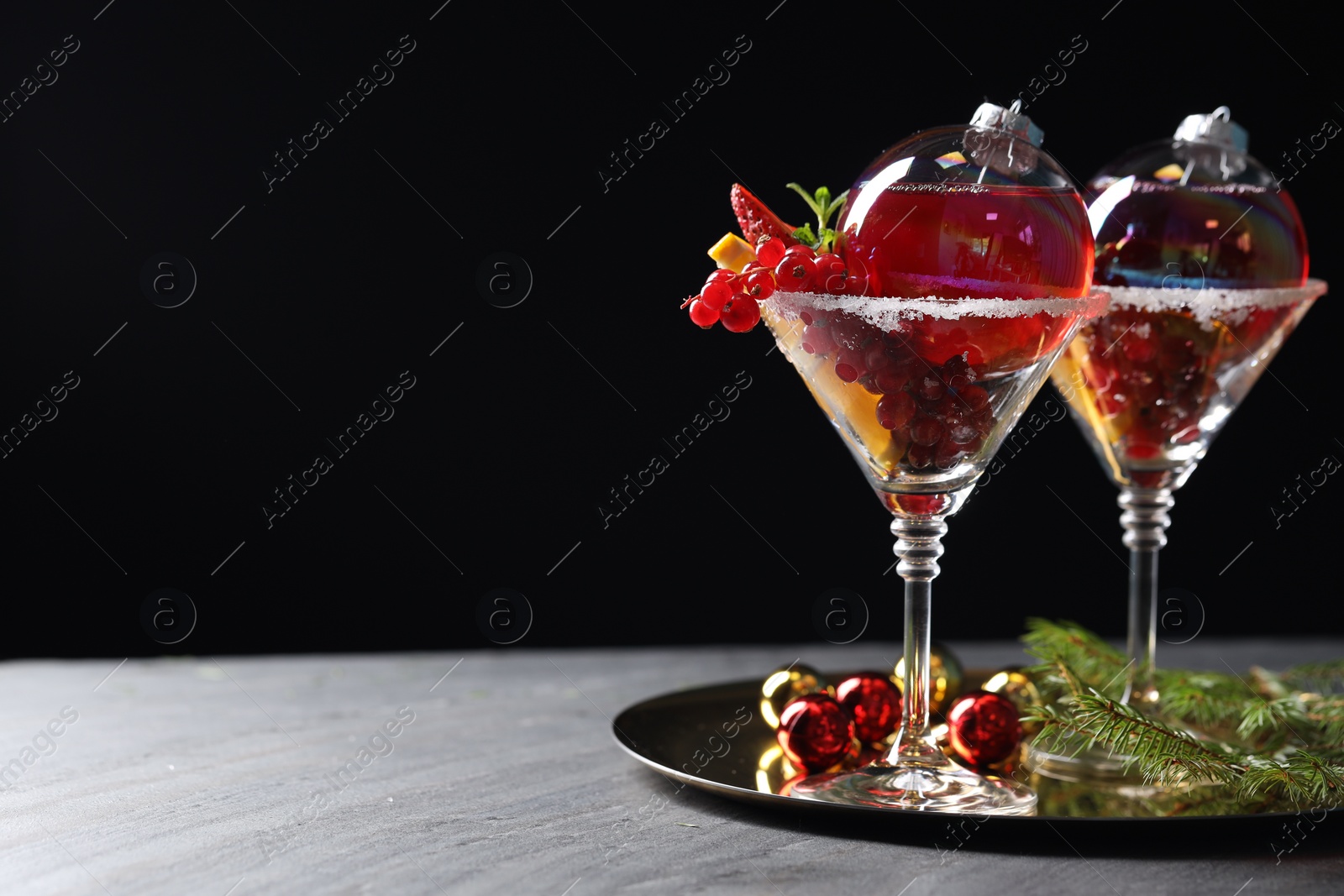 Photo of Creative presentation of Christmas Sangria cocktail in baubles and glasses on grey table against black background. Space for text