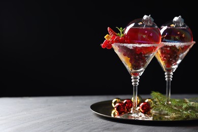 Photo of Creative presentation of Christmas Sangria cocktail in baubles and glasses on grey table against black background. Space for text