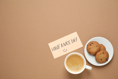 Photo of Delicious morning coffee, cookies and card with HAVE A NICE DAY wish on brown background, flat lay. Space for text