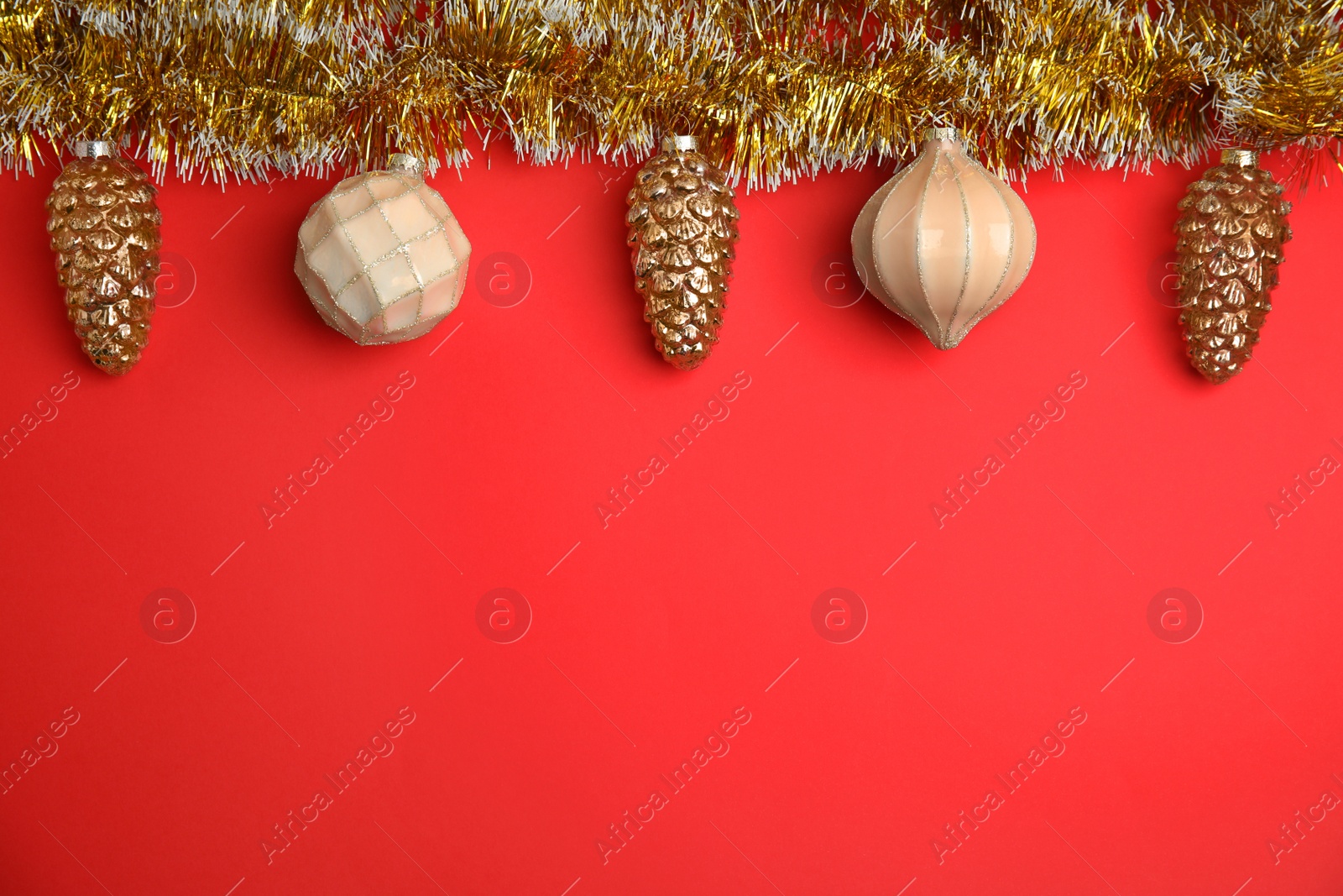 Photo of Shiny golden tinsel and Christmas baubles on red background, flat lay. Space for text