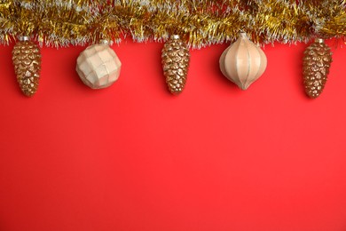 Photo of Shiny golden tinsel and Christmas baubles on red background, flat lay. Space for text