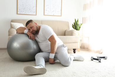 Photo of Lazy overweight man with sport equipment sleeping on floor at home